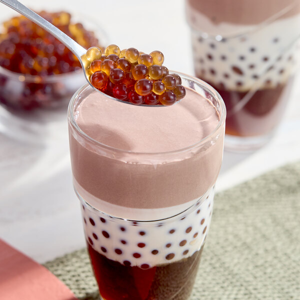 A glass of layered milk tea with coffee bursting boba pearls, with a spoonful of boba being added on top.