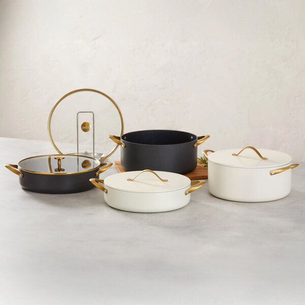 A set of round induction-ready casserole pans with covers, featuring black and white finishes and gold handles.