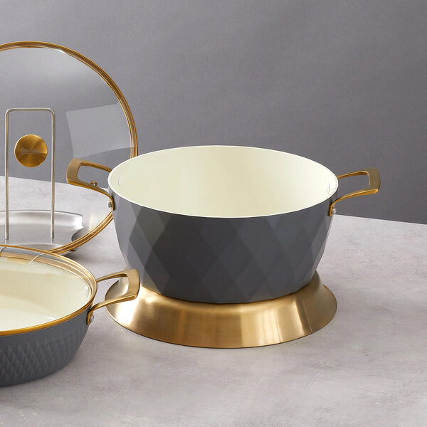 A round graphite casserole pan with gold handles and base, accompanied by a matching glass lid.