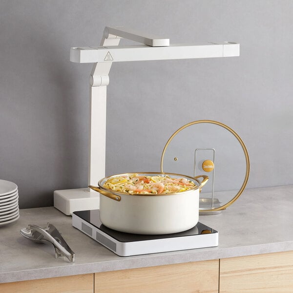 A 4-quart gold accent stainless steel insert pan with handles, shown with a glass lid and placed on an induction cooktop.