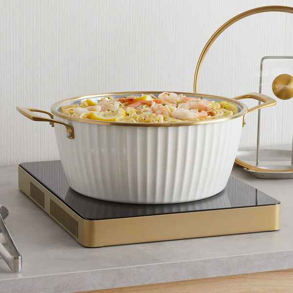 A white round induction-ready casserole pan with gold handles and a matching cover, filled with food.