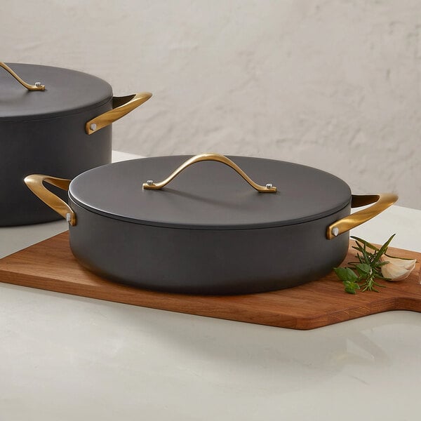 A black round induction-ready casserole pan with a lid and gold handles, holding 4 quarts.
