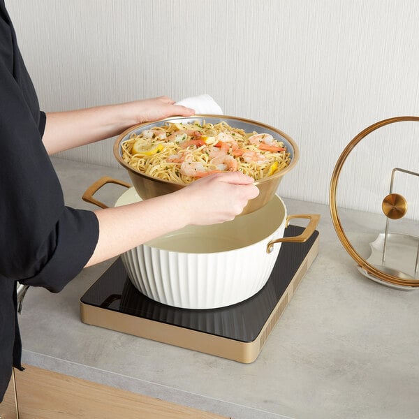 A white round induction-ready chafer casserole pan with a cover, shown in use on a countertop induction burner.
