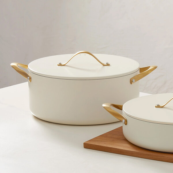 A large ivory round casserole pan with a lid and gold handles, designed for induction cooking.