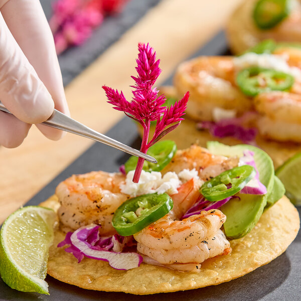 A plate of shrimp tostadas garnished with Fresh Origins Firestix edible flowers, avocado, jalapeño, cabbage, and lime wedges.