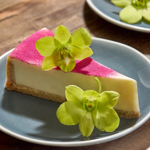 A slice of cheesecake garnished with two green edible orchids on a blue plate.