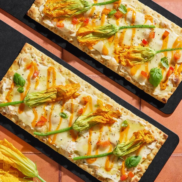 A pair of flatbreads topped with cheese, diced red peppers, basil leaves, and Fresh Origins squash blossom edible flowers.