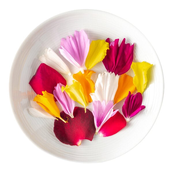 A white plate containing a colorful assortment of edible flower petals in red, yellow, pink, orange, and white.