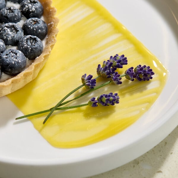 A plate with a blueberry tart, a yellow sauce, and sprigs of Fresh Origins lavender edible flowers.
