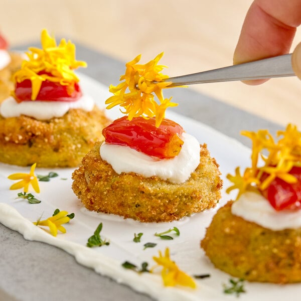 A plate of breaded appetizers topped with cream, roasted tomato, and Fresh Origins Micro Marigold edible flowers.