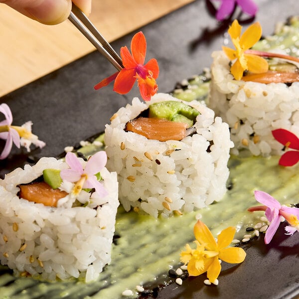 A plate of sushi rolls garnished with colorful Fresh Origins Micro Orchid edible flowers.