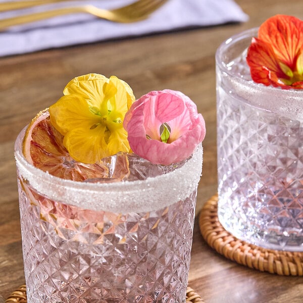 A glass of beverage garnished with colorful edible hibiscus flowers and a sugared rim.