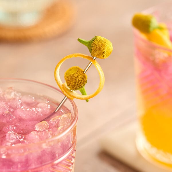 A cocktail garnished with Fresh Origins Buzz Button edible flowers and a twist of citrus peel on a metal pick.