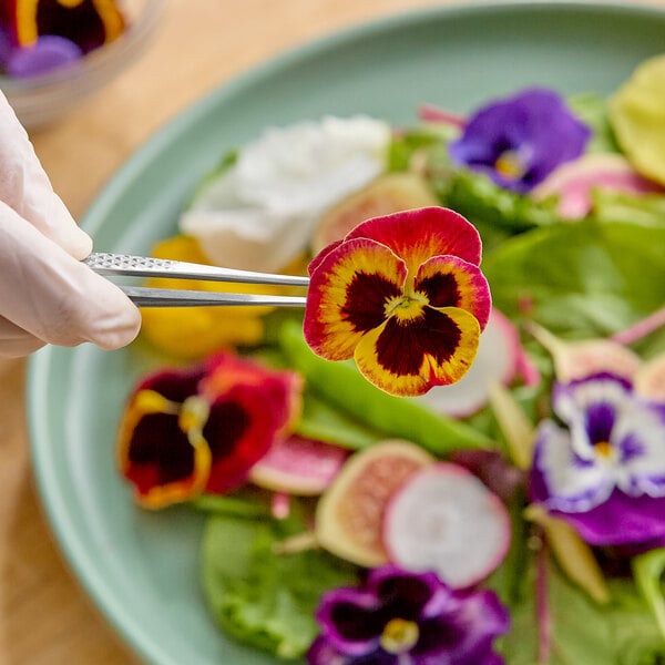 A plate of assorted Fresh Origins pansy edible flowers being arranged with tweezers.