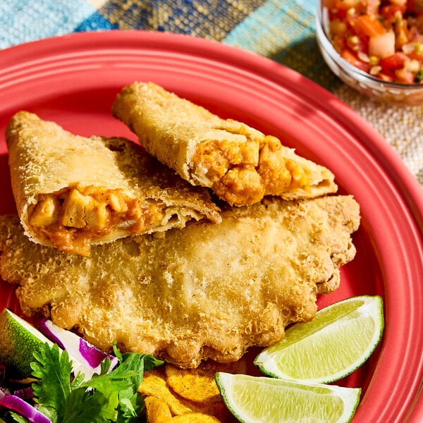 An empanada filled with chicken and cheese, served on a red plate with lime wedges and garnish.