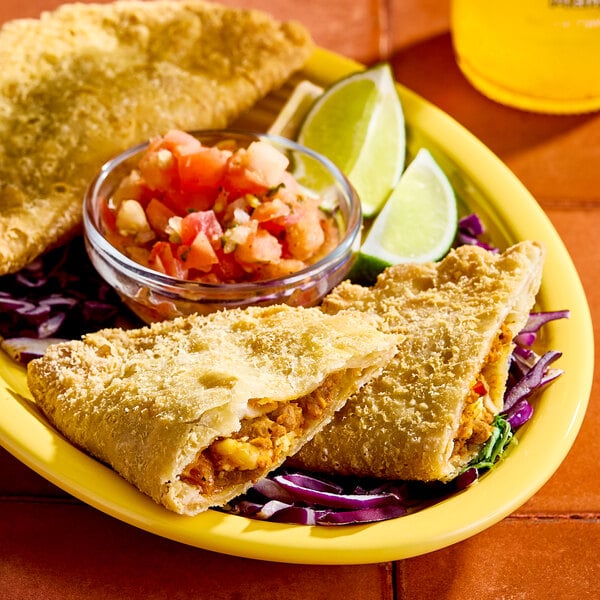 An El Monterey beef and cheese empanada served on a plate with lime wedges, shredded cabbage, and a side of salsa.