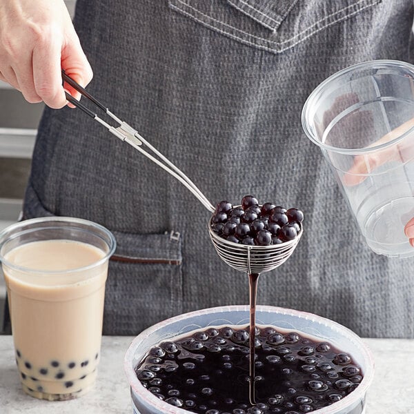 A stainless steel wire boba scoop with a black coated handle being used to serve tapioca pearls.