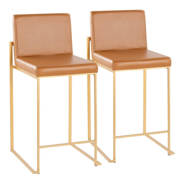 A pair of counter height stools with gold metal frames and camel faux leather seats and backs.