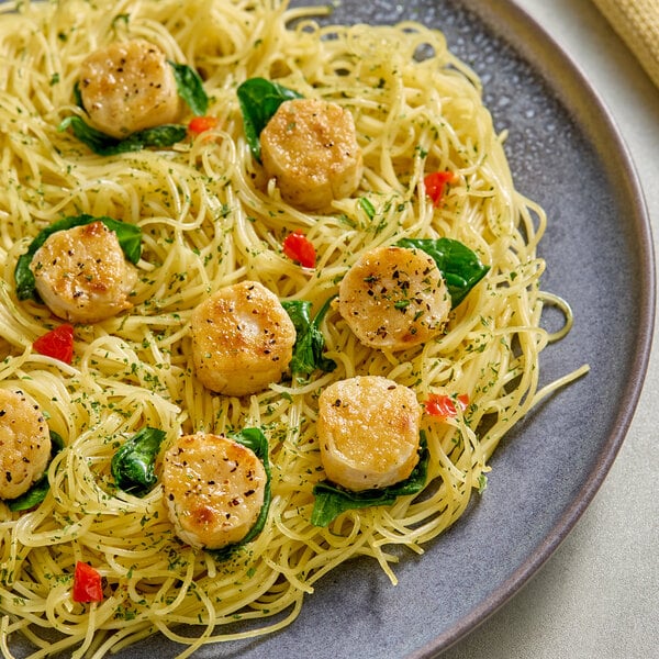 A plate of pasta topped with plant-based vegan dusted scallops and garnished with herbs and vegetables.