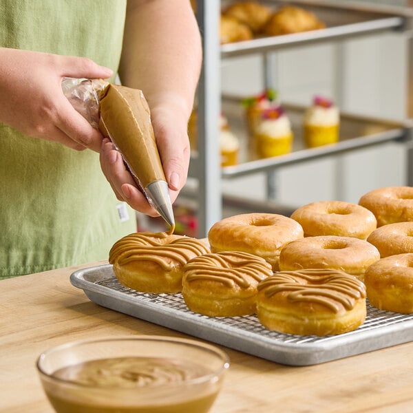 A person piping maple icing onto donuts on a cooling rack.