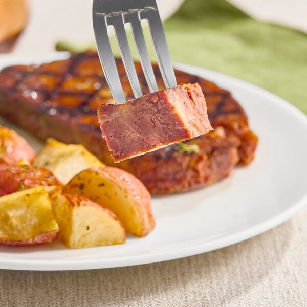 A plate with a plant-based filet mignon and roasted potatoes, with a fork holding a piece of the filet.