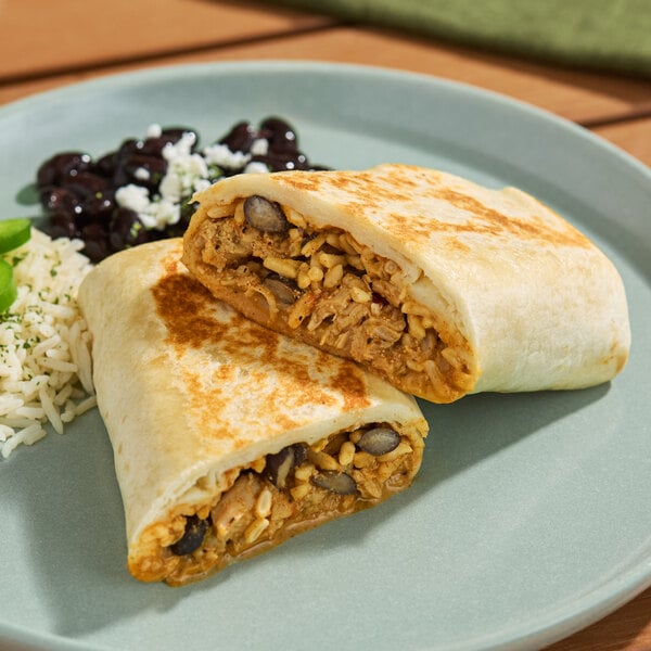 A chicken fajita burrito cut in half, served on a plate with rice and black beans.