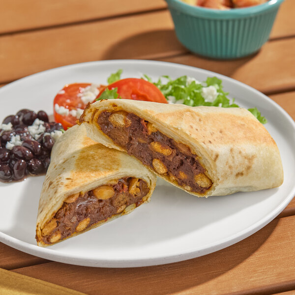 A beef burrito cut in half, served on a plate with black beans, lettuce, and tomato.