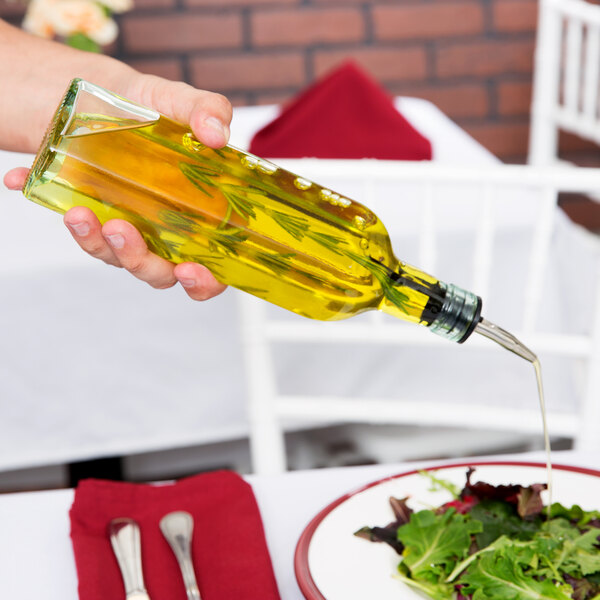 A glass olive oil cruet with a pourer being used to drizzle oil onto a salad.