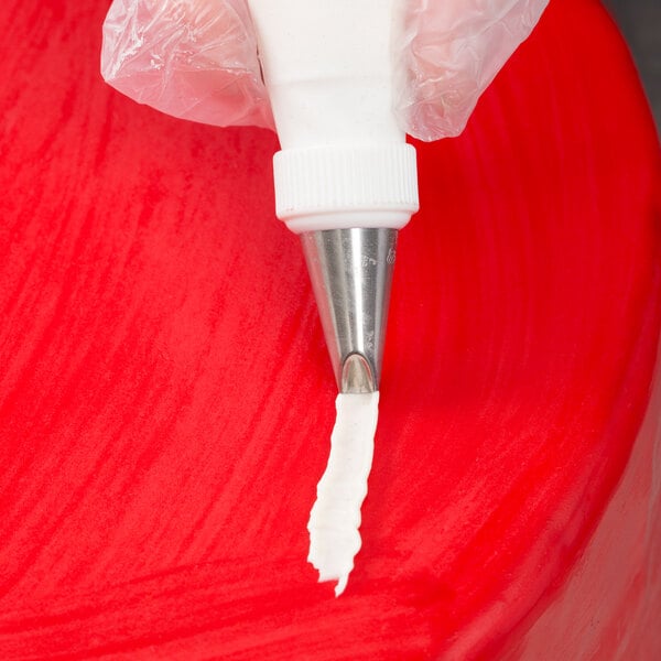 A metal piping tip being used to apply white icing onto a red surface.