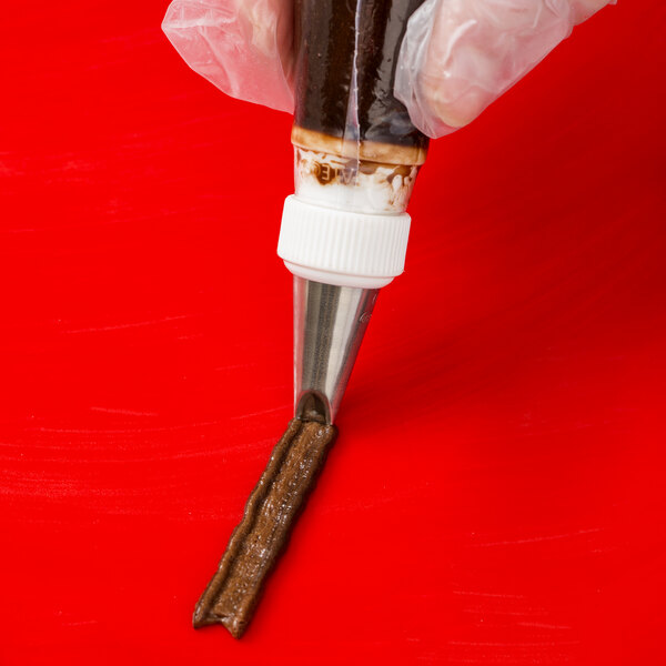 A metal piping tip being used to pipe chocolate icing onto a red surface.