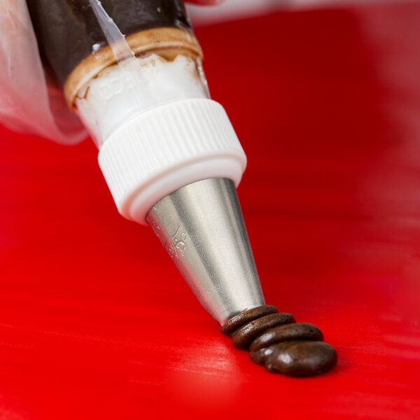 A metal piping tip attached to a piping bag being used to pipe chocolate icing onto a red surface.