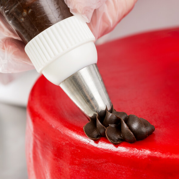 A metal piping tip being used to apply chocolate frosting onto a red cake.