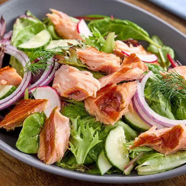 A salad topped with pieces of honey smoked salmon, red onion, cucumber, radish, and fresh greens.
