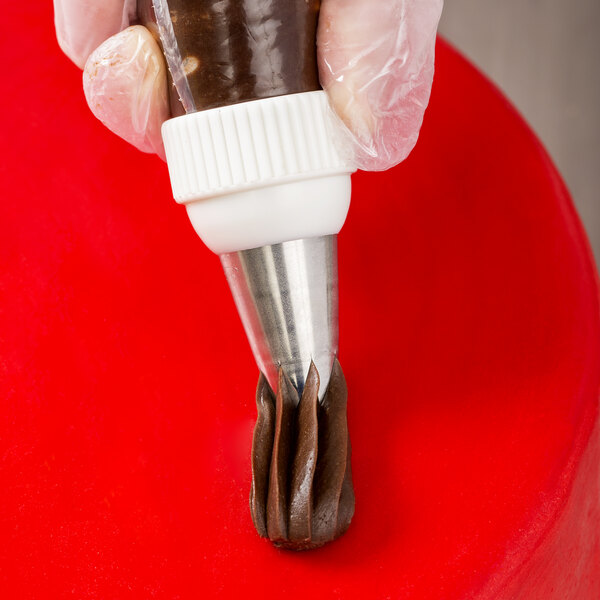 A metal piping tip being used to pipe chocolate frosting onto a red surface.