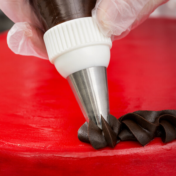 A close-up of a gloved hand using an Ateco swirl top piping tip to apply chocolate frosting onto a red cake surface.