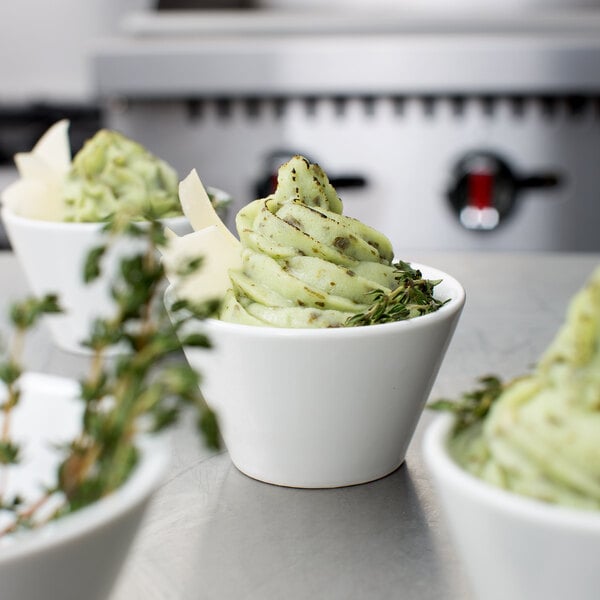 A white bowl filled with green swirled mashed potatoes garnished with herbs and cheese, piped using the Ateco Swirl Top Piping Tip 885.