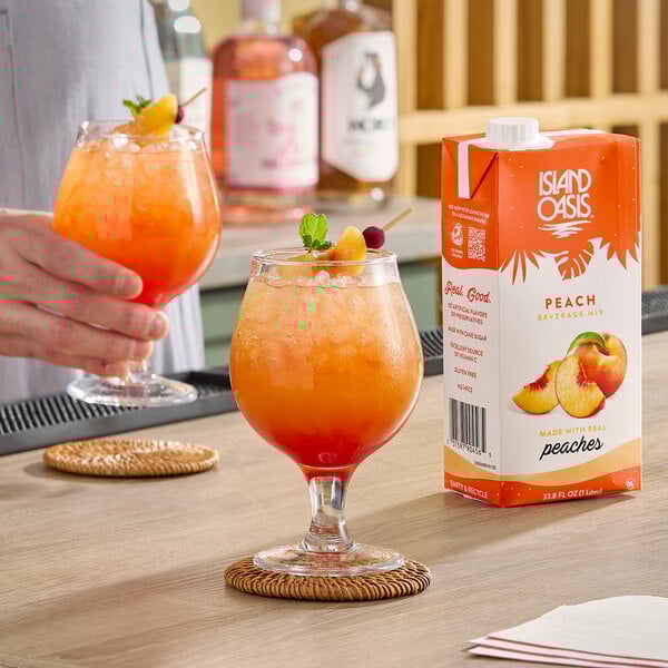 A carton of Island Oasis Peach Beverage Mix next to a glass of peach-colored iced drink garnished with fruit.