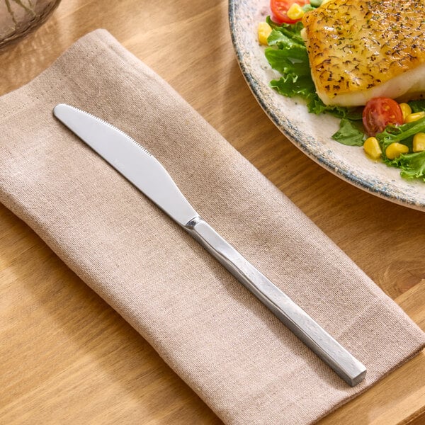 A stainless steel dinner knife with a modern, squared handle resting on a beige napkin.