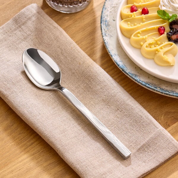 A stainless steel teaspoon with a modern, forged design resting on a beige napkin.