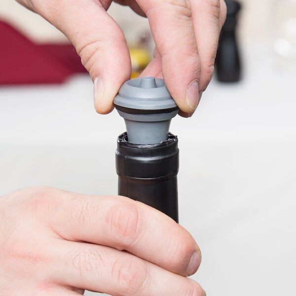A person inserting a gray Vacu Vin replacement wine stopper into the neck of a wine bottle.