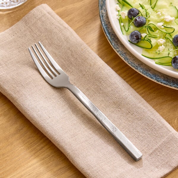 A stainless steel salad fork with a textured handle resting on a beige napkin.