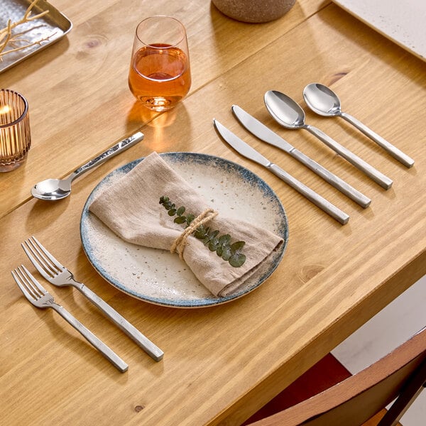 An extra heavy weight stainless steel salad fork with a modern, squared handle design placed on a wooden dining table.