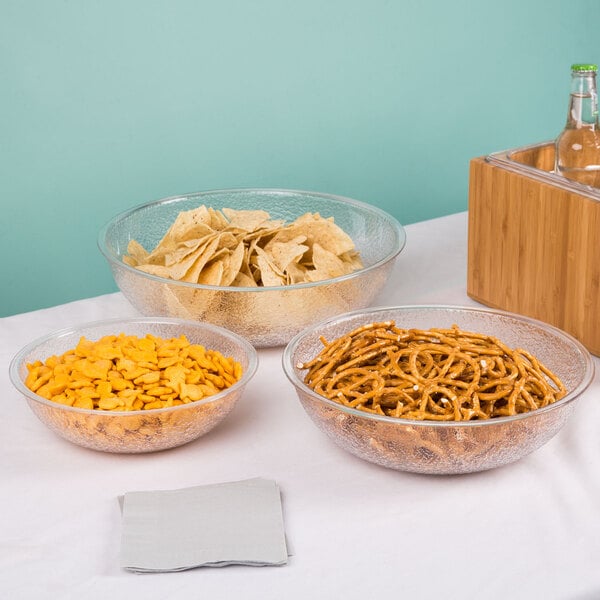A translucent pebbled polycarbonate serving bowl filled with tortilla chips, shown alongside similar bowls with snacks.