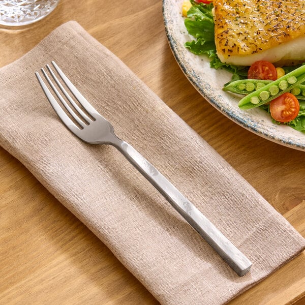A stainless steel dinner fork with a textured handle resting on a beige napkin.