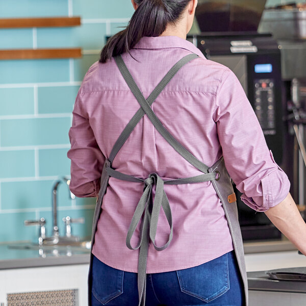 A pair of gray cross-back replacement apron straps shown tied on a person in a kitchen setting.