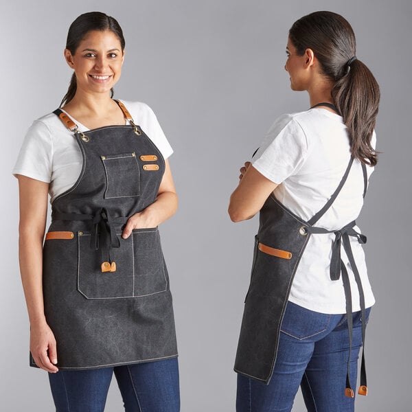 A black heavy weight canvas cross-back bib apron with three pockets and leather accents, shown from the front and back.