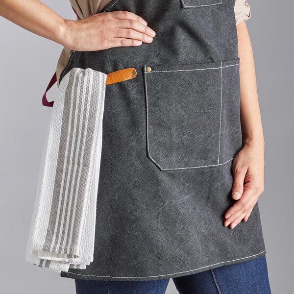 A black heavy weight canvas cross-back bib apron with three pockets, shown with a towel hanging from a side loop.