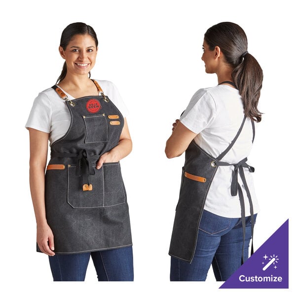 A black heavy weight canvas cross-back bib apron with three pockets, shown from the front and back, worn by a person over a white shirt and jeans.