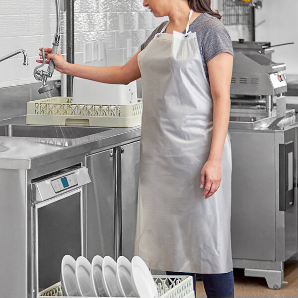 A person wearing a clear vinyl dishwasher apron while working in a commercial kitchen.