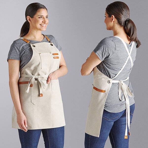 A cream-colored heavy weight canvas cross-back bib apron with three pockets, shown from the front and back on a person.